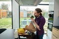 Handsome European man holding greens while unpacking eco paper bag with healthy food, standing at kitchen countertop in a spacious Royalty Free Stock Photo