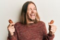 Handsome caucasian man with long hair eating chicken wings winking looking at the camera with sexy expression, cheerful and happy