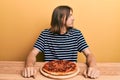 Handsome caucasian man with long hair eating tasty pepperoni pizza looking to side, relax profile pose with natural face with