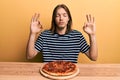 Handsome caucasian man with long hair eating tasty pepperoni pizza relax and smiling with eyes closed doing meditation gesture