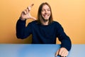 Handsome caucasian man with long hair wearing casual clothes sitting on the table smiling and confident gesturing with hand doing Royalty Free Stock Photo