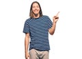 Handsome caucasian man with long hair wearing casual striped t-shirt with a big smile on face, pointing with hand and finger to Royalty Free Stock Photo