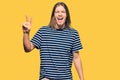 Handsome caucasian man with long hair wearing casual striped t-shirt smiling with happy face winking at the camera doing victory Royalty Free Stock Photo
