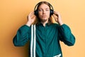 Handsome caucasian man with long hair wearing gym clothes and using headphones relaxed with serious expression on face Royalty Free Stock Photo