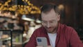 Man programmer sending messages on the smartphone, while working at the cafe.