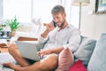 Handsome caucasian man smiling happy sitting on the sofa using computer laptop speaking on the phone Royalty Free Stock Photo