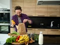 Handsome Caucasian man unpacking purchased healthy food standing by a kitchen countertop with bottle of milk and healthy raw vegan