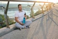 Handsome Caucasian muscular man, determined athlete, sportsman in headphones relaxing after workout outdoors at dawn, holding