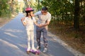 Handsome Caucasian smiling father in glasses teaching her daughter to ride skateboard family enjoying fun weekend activity