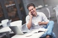 Confident young man in smart casual wear holding a cup and talking by smartphone. Royalty Free Stock Photo