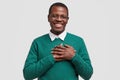 Handsome cheerful black man keeps both hands on chest, feels touched or thankful, smiles broadly, wears elegant green Royalty Free Stock Photo