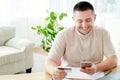 Handsome cheerful man paying with credit card on smart phone at home office, copy space. Technology, banking, business, online.