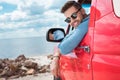 handsome cheerful man in sunglasses sitting in red car during road trip