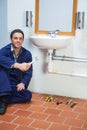 Handsome cheerful plumber sitting next to sink holding wrench Royalty Free Stock Photo