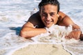 Handsome cheerful young teenager have fun at the beach on the sand and water waves looking on camera in a beautiful portrait -