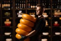 Handsome cheese sommelier with yellow wheels of cheese in shop. Worker of food cheese store carrying rounds of cheese.