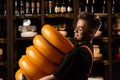 Handsome cheese sommelier with yellow wheels of cheese in shop. Worker of food cheese store carrying rounds of cheese.