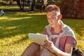 Handsome college man writing notes in copybook in campus park. Happy guy student learning outdoors sitting on grass Royalty Free Stock Photo
