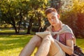 Handsome college man writing notes in copybook in campus park. Happy guy student learning outdoors sitting on grass Royalty Free Stock Photo