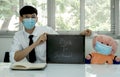 Handsome college students hold back to school banners on their desks, with dolls wearing masks instead to keep the social distance