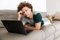 Handsome concentrated man lies on sofa using laptop