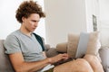 Handsome concentrated man sitting at sofa using laptop