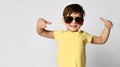 confident boy child in casual yellow t-shirt and sunglasses, smiling happily and showing two thumbs up, rejoices to win Royalty Free Stock Photo