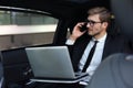 Handsome confident businessman in suit talking on smart phone and working using laptop while sitting in the car Royalty Free Stock Photo