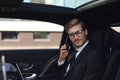 Handsome confident businessman in suit talking on smart phone and working using laptop while sitting in the car Royalty Free Stock Photo