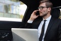 Handsome confident businessman in suit talking on smart phone and working using laptop while sitting in the car Royalty Free Stock Photo