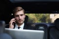Handsome confident businessman in suit talking on smart phone and working using laptop while sitting in the car Royalty Free Stock Photo