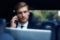 Handsome confident businessman in suit talking on smart phone and working using laptop while sitting in the car. Royalty Free Stock Photo