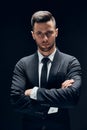 Handsome confident man in black suit with arms crossed on dark background