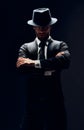 Handsome confident man in black suit and hat with arms crossed on dark background