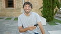 Handsome, confident young man, happily texting on his smartphone, sitting with a casual expression in the city park, enjoying a Royalty Free Stock Photo