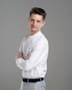 Confident young man standing in white shirt on grey background. Body profile with crosed hands