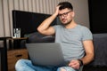 Handsome bearded confused man dressed elegant sitting on the floor at home and holding hand on head with laptop