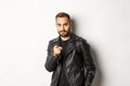 Handsome and cool bearded guy pointing finger at camera, wearing leather jacket, standing sassy against white background Royalty Free Stock Photo