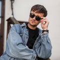 Handsome cool young man hipster straightens fashionable black sunglasses. Portrait of a handsome guy Royalty Free Stock Photo