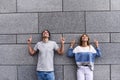 Handsome couple is pointing away and smiling, standing against gray wall. Royalty Free Stock Photo