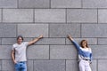 Handsome couple is pointing away and smiling, standing against gray wall. Royalty Free Stock Photo