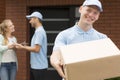 Courier in blue uniform holding big brown package and smiling