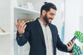 Handsome Cuban bearded businessman in a suit holding his phone in one hand, gesturing with the other, and grinning. Royalty Free Stock Photo