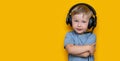 Handsome cute blonde little boy three years old in gaming black headphones. look at camera, grey eyes and grey t-shirt on yellow Royalty Free Stock Photo