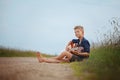 Handsome cute boy is playing on acoustic guitar sittingon road in summer day.