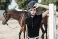 Handsome cute rider standing near brown hourse. Blurred background Royalty Free Stock Photo