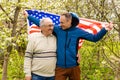 Handsome dad with his little cute sun are laying on green grassy lawn on American flag with American football ball in Royalty Free Stock Photo