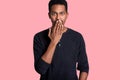 Handsome dark skinned man covers mouth with hand isolated on pink background. Guy hears shocked news from his friend. Good looking Royalty Free Stock Photo