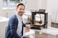 Handsome delighted man sitting near the 3d printer