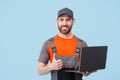 Handsome smiling delivery man in uniform with laptop looking at camera on blue background Royalty Free Stock Photo